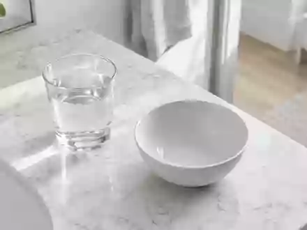 Ein minimalistisches Badezimmer-Interieur mit einem Glas Wasser auf einem weißen Marmorwaschtisch bei natürlichem Licht. - Foto: über boerse-global.de