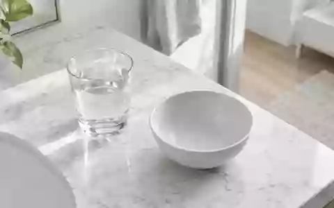 Ein minimalistisches Badezimmer-Interieur mit einem Glas Wasser auf einem weißen Marmorwaschtisch bei natürlichem Licht. - Foto: über boerse-global.de