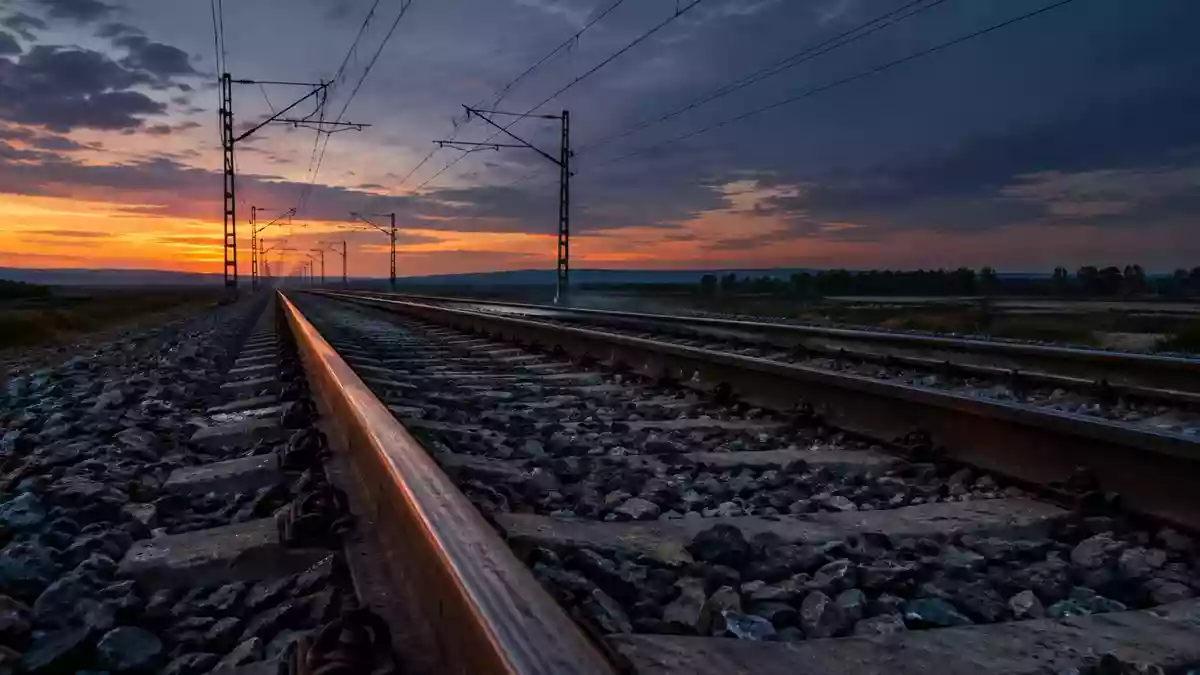 Leere Bahngleise bei Dämmerung mit Oberleitungen im Hintergrund. Illustration mit AI erstellt.