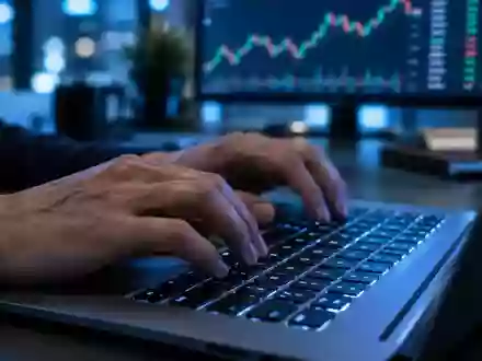 Person tippt an einem Laptop in einem abgedunkelten Büro mit Fokus auf die Hände vor einem unscharfen Monitor. - Foto: über boerse-global.de