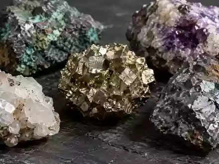 Nahaufnahme von rohen Mineralproben und Erzgestein auf einer dunklen, texturierten Industriefläche. - Foto: über boerse-global.de