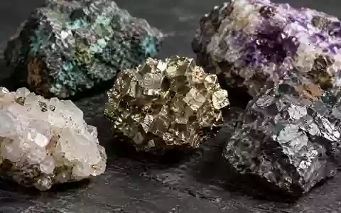 Nahaufnahme von rohen Mineralproben und Erzgestein auf einer dunklen, texturierten Industriefläche. - Foto: über boerse-global.de