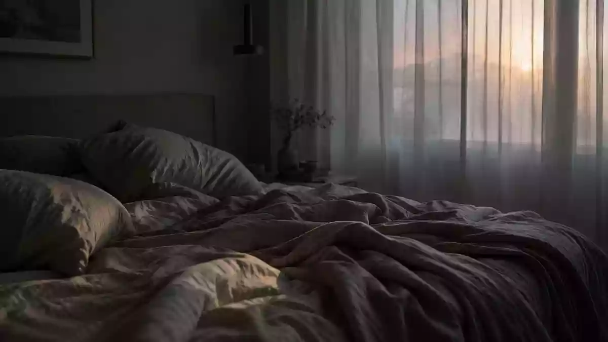 Ein ungemachtes Bett in einem ruhig beleuchteten Schlafzimmer im morgendlichen Licht. Illustration mit AI erstellt.