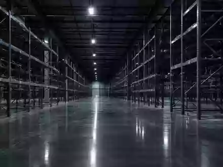 Weitläufiges, leeres Logistiklager mit hohen Metallregalen und reflektierendem Betonboden in einer kühlen, sterilen Atmosphäre. - Foto: über boerse-global.de