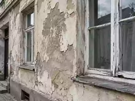 Fassade eines sanierungsbedürftigen Wohnhauses mit sichtbaren Schäden am Fensterrahmen und Putz. - Foto: über boerse-global.de