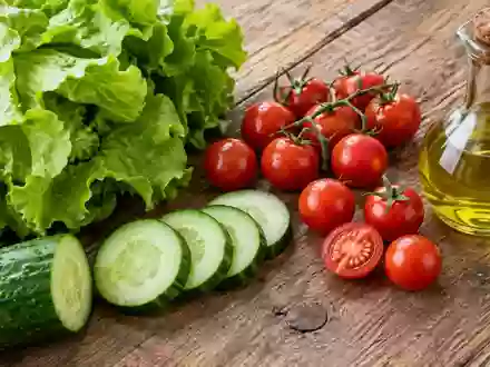 Frische Zutaten wie Salat, Gurken und Tomaten sowie eine kleine Ölflasche auf einem rustikalen Holztisch. - Foto: über boerse-global.de