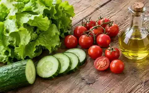 Frische Zutaten wie Salat, Gurken und Tomaten sowie eine kleine Ölflasche auf einem rustikalen Holztisch. - Foto: über boerse-global.de