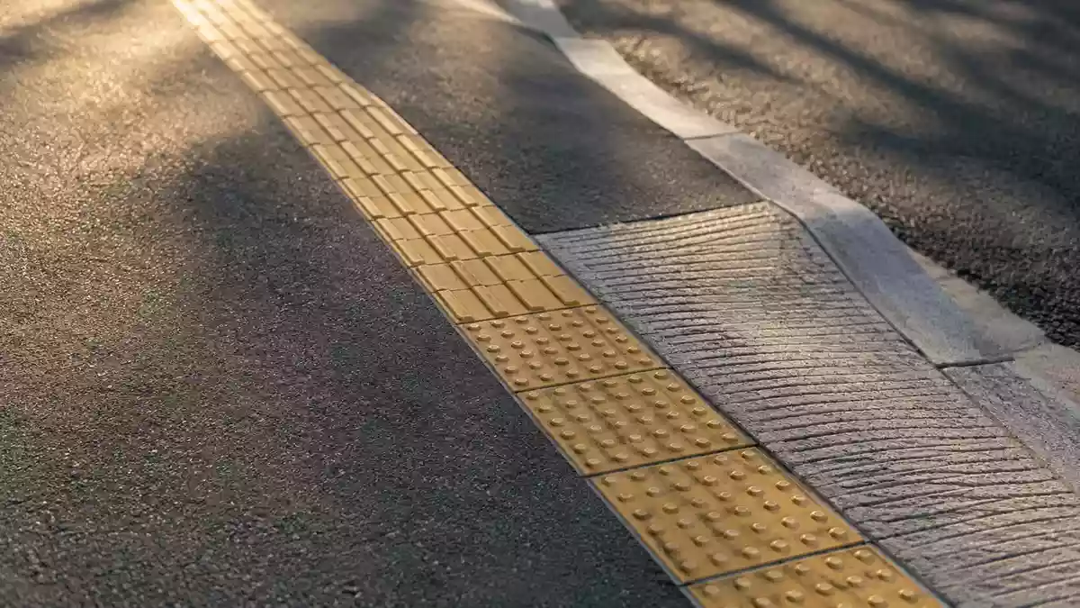 Ein leerer Gehweg mit einer abgesenkten Bordsteinkante und taktilen Leitplatten bei natürlichem Tageslicht. Illustration mit AI erstellt.