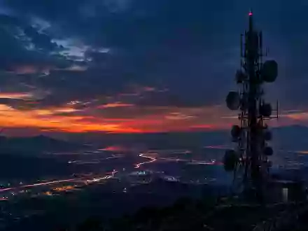 Eine weitläufige Mobilfunkantenne bei Dämmerung über einer nächtlichen Stadtlandschaft. - Foto: über boerse-global.de