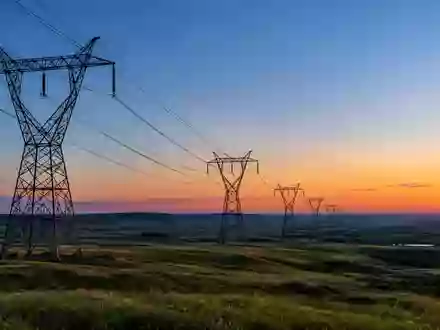 Hochspannungsmasten in einer weitläufigen Industrielandschaft bei Dämmerung als Symbol für Energieinfrastruktur. - Foto: über boerse-global.de