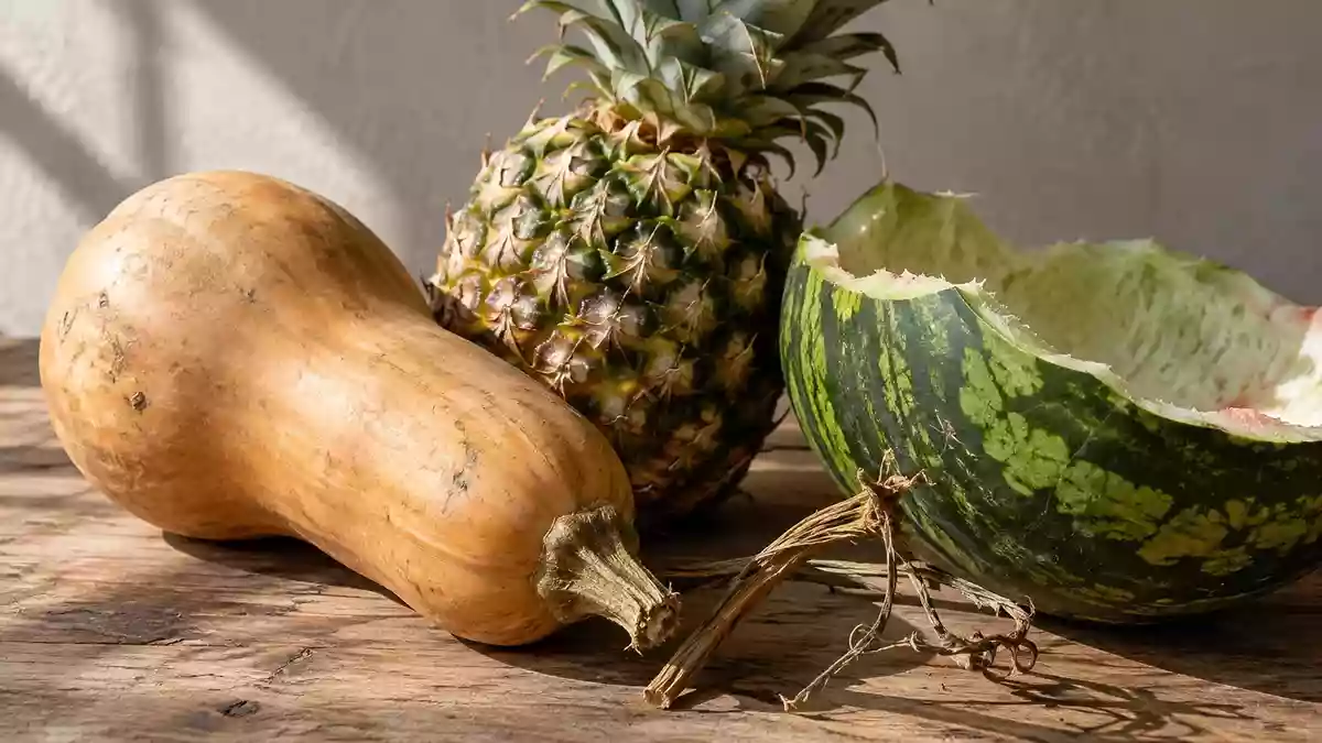 Nahaufnahme von verschiedenen Obst- und Gemüseresten wie Kürbisschalen und Ananasschalen auf einer rustikalen Holzoberfläche. Illustration mit AI erstellt.