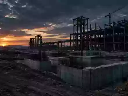 Eine weitläufige, verlassene Industriebaustelle mit massiven Betonfundamenten und Stahlgerüsten in der Dämmerung. - Foto: über boerse-global.de
