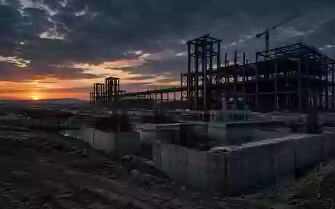 Eine weitläufige, verlassene Industriebaustelle mit massiven Betonfundamenten und Stahlgerüsten in der Dämmerung. - Foto: über boerse-global.de