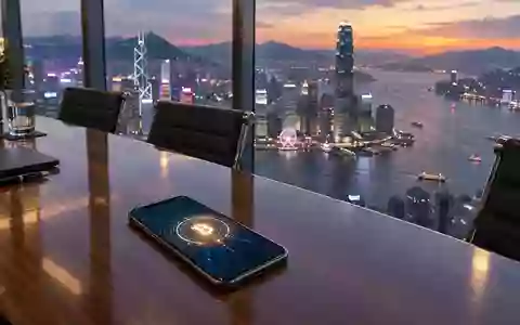 Ein Smartphone mit einem digitalen Währungssymbol in einem modernen Konferenzraum mit Blick auf die Skyline von Hongkong. - Foto: über boerse-global.de