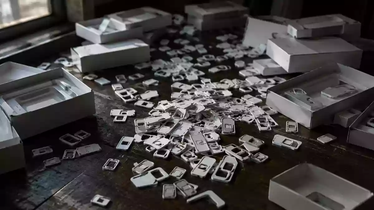 Eine Ansammlung von leeren SIM-Karten-Rahmen und Verpackungsmaterial auf einem dunklen Holztisch. Illustration mit AI erstellt.