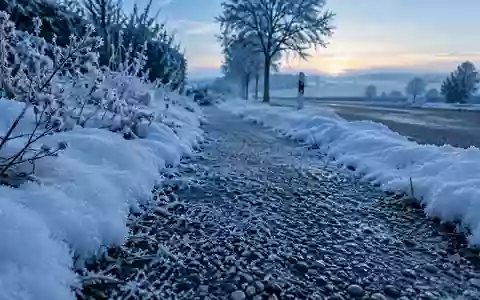 Verschneiter Gehweg an einem frostigen Wintermorgen in einer Wohngegend mit gefrorenem Streugut auf dem Boden. - Foto: über boerse-global.de
