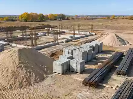 Eine Baustelle mit aufgeschüttetem Bausand, gestapelten Mauersteinen und Bewehrungsstahl auf einer vorbereiteten Baufläche. - Foto: über boerse-global.de