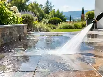Ein sauberer Fliesenboden auf einer Terrasse wird mit einem Hochdruckreiniger gereinigt, wobei Wassertropfen im Sonnenlicht glänzen. - Foto: über boerse-global.de