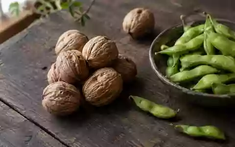 Nahaufnahme von Walnüssen in der Schale und grünen Edamame-Schoten auf einem rustikalen Holztisch bei natürlichem Licht. - Foto: über boerse-global.de