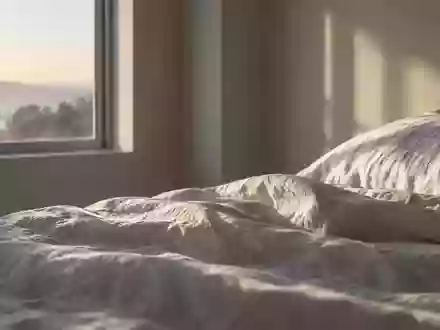Ein minimalistisches, ruhiges Schlafzimmer bei Tagesanbruch mit Fokus auf die Textur der Bettwäsche und natürliches Licht. - Foto: über boerse-global.de