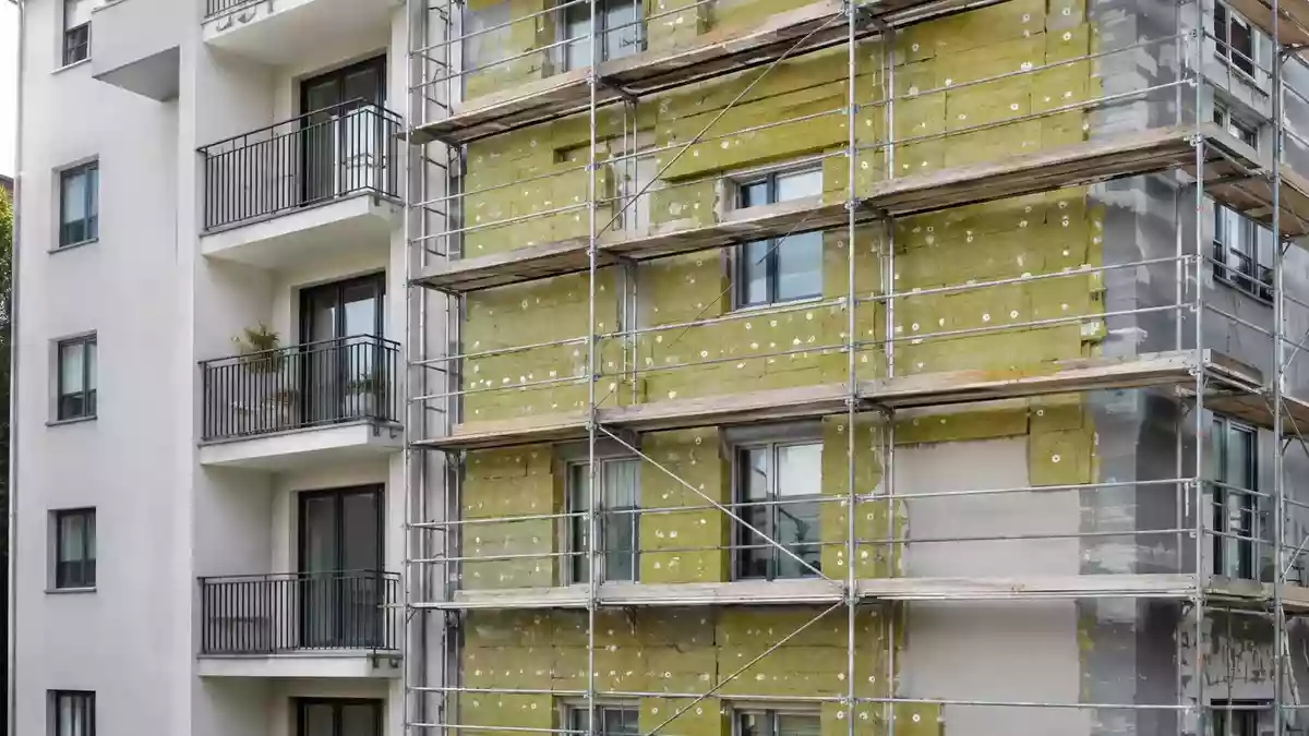 Fassade eines Wohngebäudes während einer energetischen Sanierung mit sichtbarer Wärmedämmung und Gerüst. Illustration mit AI erstellt.