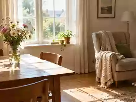 Ein sonnendurchflutetes Wohnzimmer mit einem Holztisch, einer Blumenvase und einem gemütlichen Sessel mit Decke. - Foto: über boerse-global.de