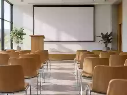 Ein leerer, modern eingerichteter Seminarraum mit einem hölzernen Rednerpult und einer weißen Projektionsfläche. - Foto: über boerse-global.de