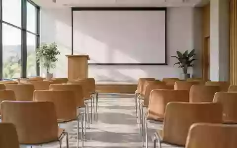 Ein leerer, modern eingerichteter Seminarraum mit einem hölzernen Rednerpult und einer weißen Projektionsfläche. - Foto: über boerse-global.de