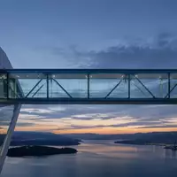 Eine moderne Glas-Stahl-Brücke bei Dämmerung, die zwei abstrakte architektonische Strukturen verbindet. - Foto: über boerse-global.de