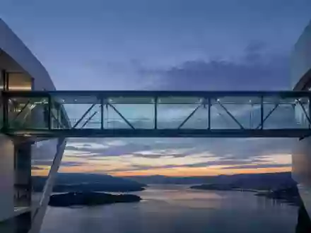 Eine moderne Glas-Stahl-Brücke bei Dämmerung, die zwei abstrakte architektonische Strukturen verbindet. - Foto: über boerse-global.de