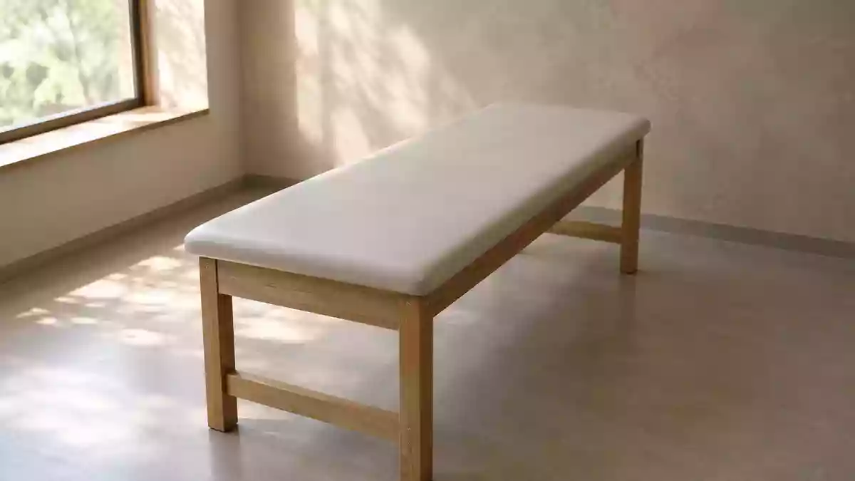 Ein minimalistischer, leerer Behandlungsraum in einer Klinik mit einer hölzernen Untersuchungsliege in weichem Tageslicht. Illustration mit AI erstellt.