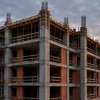 Eine Baustelle mit einem im Rohbau befindlichen Wohngebäude aus Beton und Stahl bei Dämmerung. - Foto: über boerse-global.de