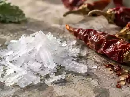 Kristalline Menthol-Flocken neben getrockneten Chilischoten auf einer steinernen Oberfläche. - Foto: über boerse-global.de
