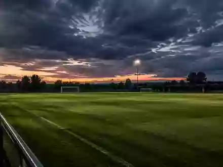 Ein leerer Fußballtrainingsplatz bei Dämmerung mit langen Schatten auf dem Rasen und dramatischem Himmel. - Foto: über boerse-global.de
