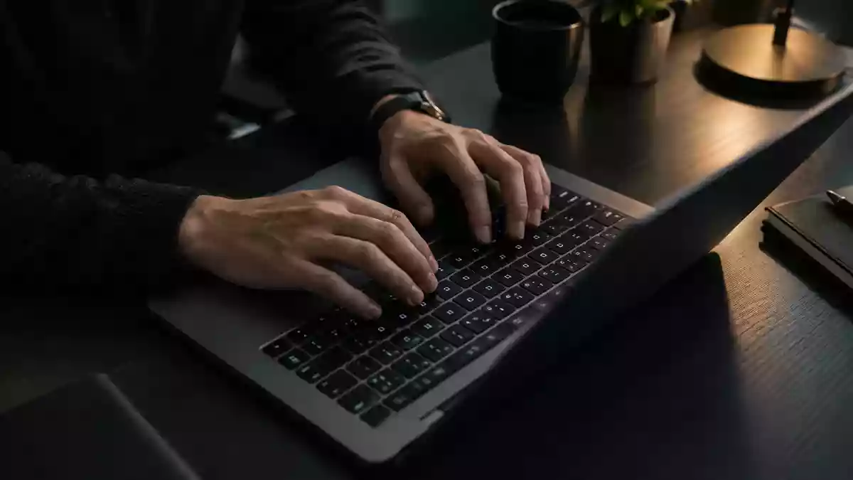 Nahaufnahme von Händen an einer Laptop-Tastatur in einem abgedunkelten Büro. Illustration mit AI erstellt.