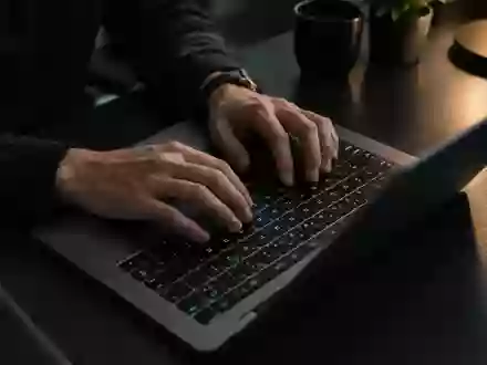 Nahaufnahme von Händen an einer Laptop-Tastatur in einem abgedunkelten Büro. - Foto: über boerse-global.de