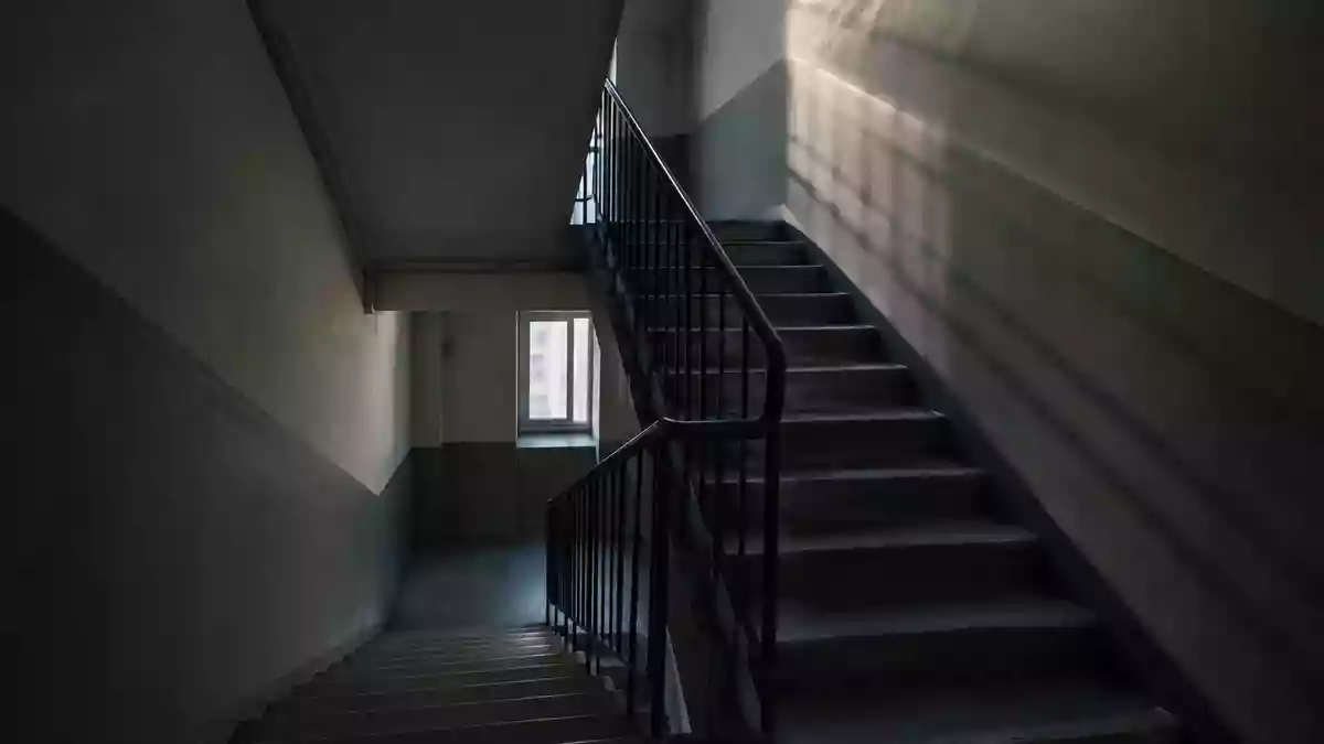 Ein schmales, schattiges Treppenhaus in einem Wohngebäude mit Betonstufen und Metallgeländer. Illustration mit AI erstellt.