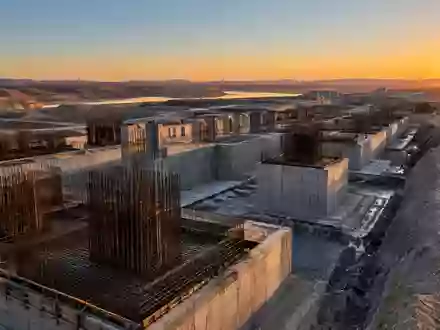 Eine weitläufige Baustelle für großflächige Infrastruktur mit massiven Betonfundamenten und Stahlträgern im Dämmerlicht. - Foto: über boerse-global.de