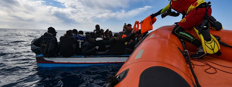 Mehrere Migranten sitzen in einem Boot im Mittelmeer während Rettungskräfte versuchen ihnen zu helfen. - Foto: Antonio Sempere/EUROPA PRESS/dpa