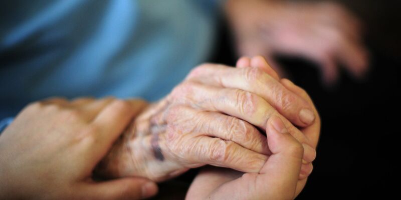 Eine Pflegekraft hält in einem Seniorenheim die Hand einer Bewohnerin. Die Pflegeversicherung sieht sich mit einem Defizit konfrontiert. - Foto: Daniel Reinhardt/dpa