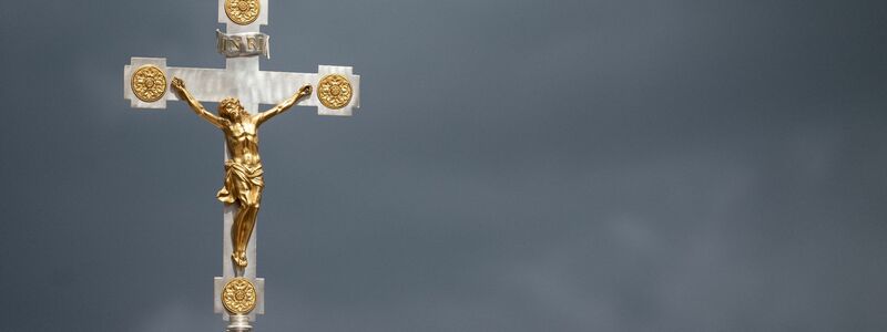 Dunkle Wolken über einem Kruzifix: Immer mehr Menschen nehmen Abstand von der Katholischen Kirche. - Foto: Marijan Murat/dpa