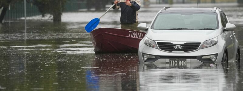 Ein Mann paddelt mit seinem Boot auf einer überfluteten Straße am Stadtrand von Sydney. - Foto: Mark Baker/AP/dpa