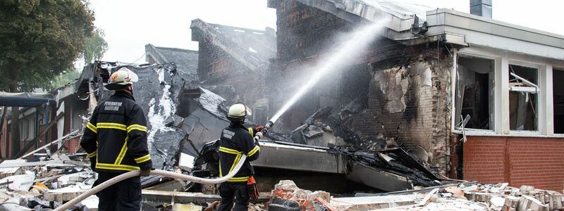 Polizisten stehen hinter einem Metallbehälter. Trümmerteile sollen bei dem Brand Hunderte Meter weit geflogen sein.  - Foto: Daniel Bockwoldt/dpa