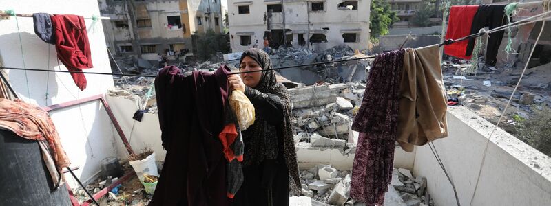 Eine Frau steht in den Trümmern eines durch israelischen Luftangriff beschädigten Gebäudes in Gaza und hängt Wäsche über eine Leine. - Foto: Ashraf Amra/APA Images via ZUMA Press Wire/dpa