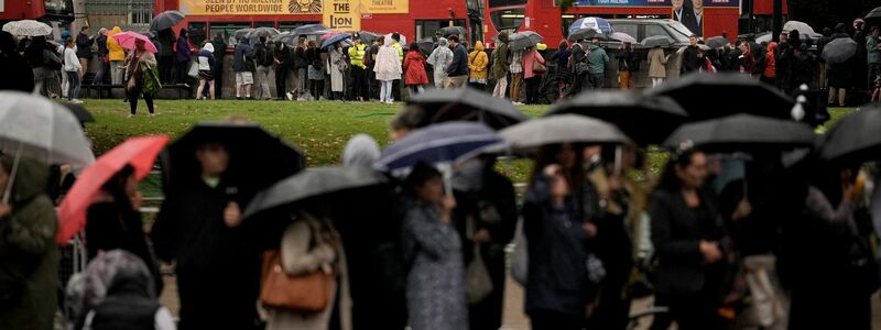 Menschen stehen auf der Straße und warten auf den Leichenwagen mit dem Sarg von Königin Elizabeth II. - Foto: Andreea Alexandru/AP/dpa