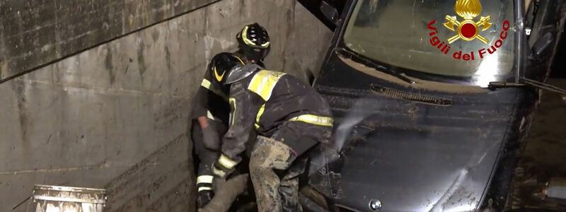 Feuerwehrleute schieben einen Schlauch in eine Tiefgarage, die durch ein hochgestelltes Auto versperrt ist. - Foto: -/Vigili del Fuoco/dpa