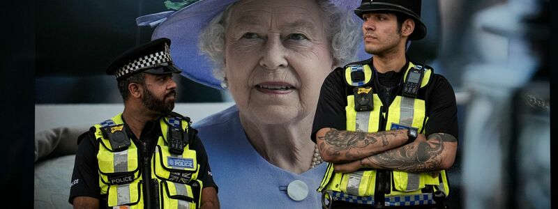 Polizisten stehen vor einem Bild von Königin Elizabeth II. in London. - Foto: Vadim Ghirda/AP/dpa