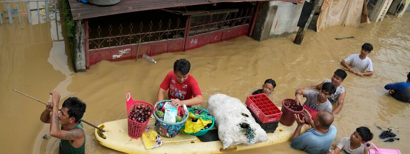 Anwohner verschenken Zwiebeln und andere Lebensmittel am Hilfsbedürftige entlang einer durch den Taifun Noru überfluteten Straße im philippinischen San Miguel. - Foto: Aaron Favila/AP/dpa