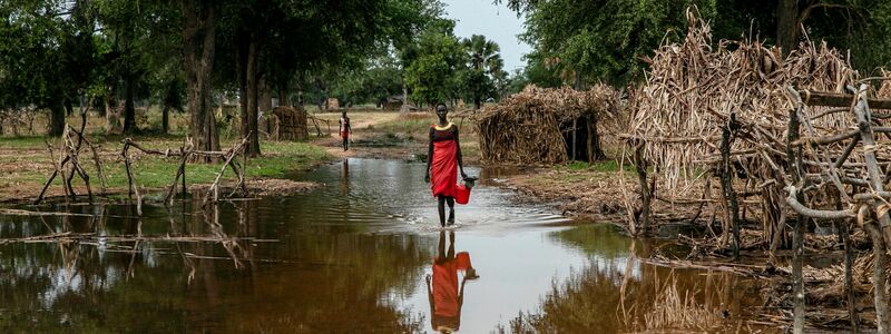Eine Frau watet durch das Hochwasser zwischen verlassenen Unterkünften im Dorf Majak Awar im Südsudan. Dort sind ganze Bundesstaaten überflutet. Sieben der zehn Klimakrisenherde, die die Nichtregierungsorganisation Oxfam in einer aktuellen Studie identifiziert hat, liegen in Afrika. - Foto: Adrienne Surprenant/AP/dpa
