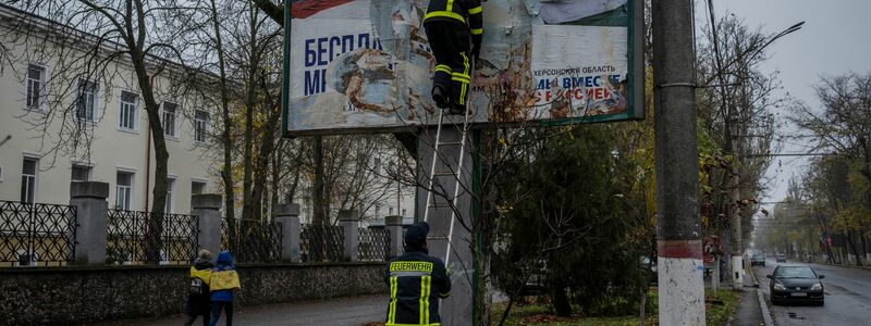 Feuerwehrleute entfernen russische Plakate in Cherson. - Foto: Bernat Armangue/AP/dpa
